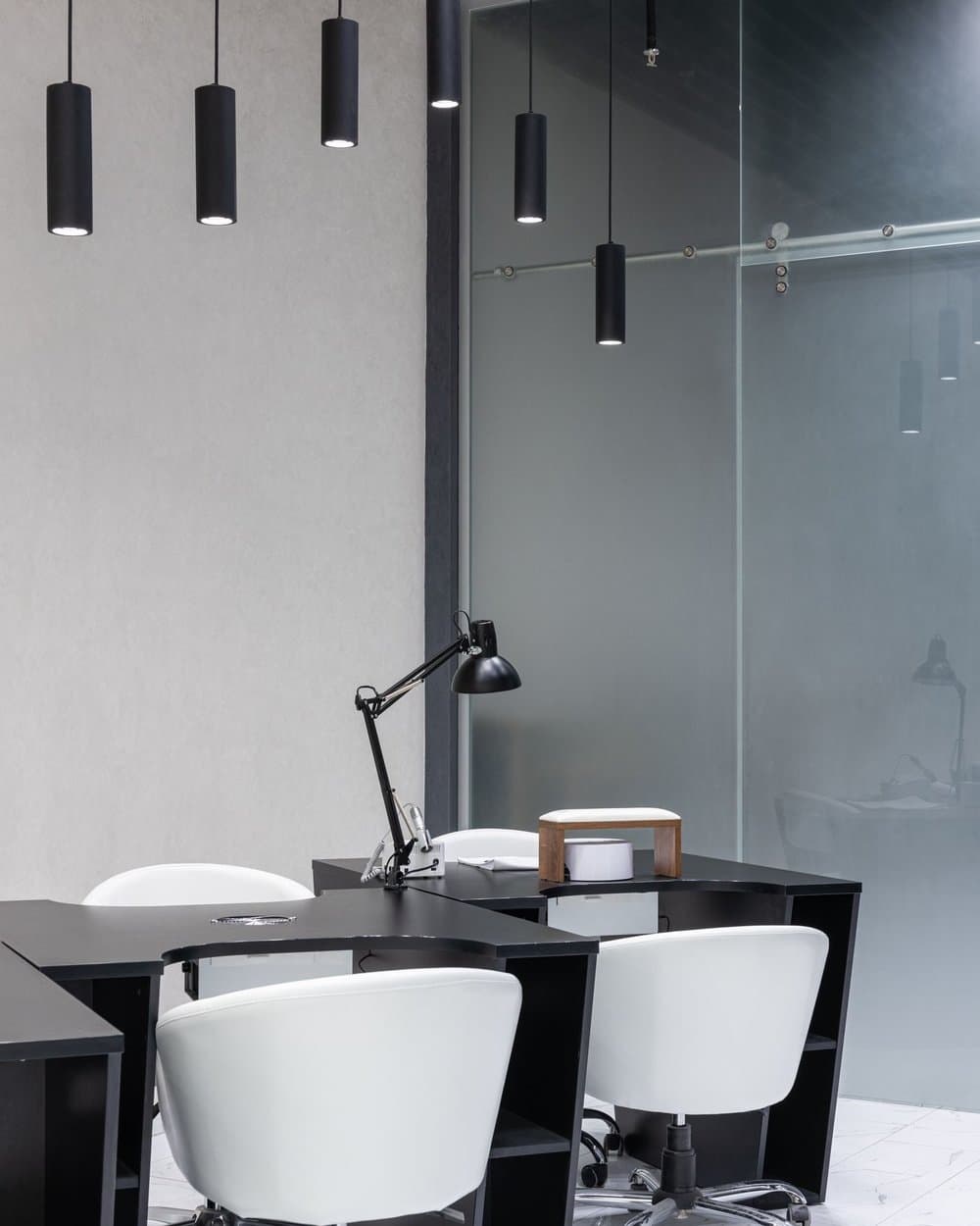 Modern office workspace beneath slim black cylindrical pendant downlights