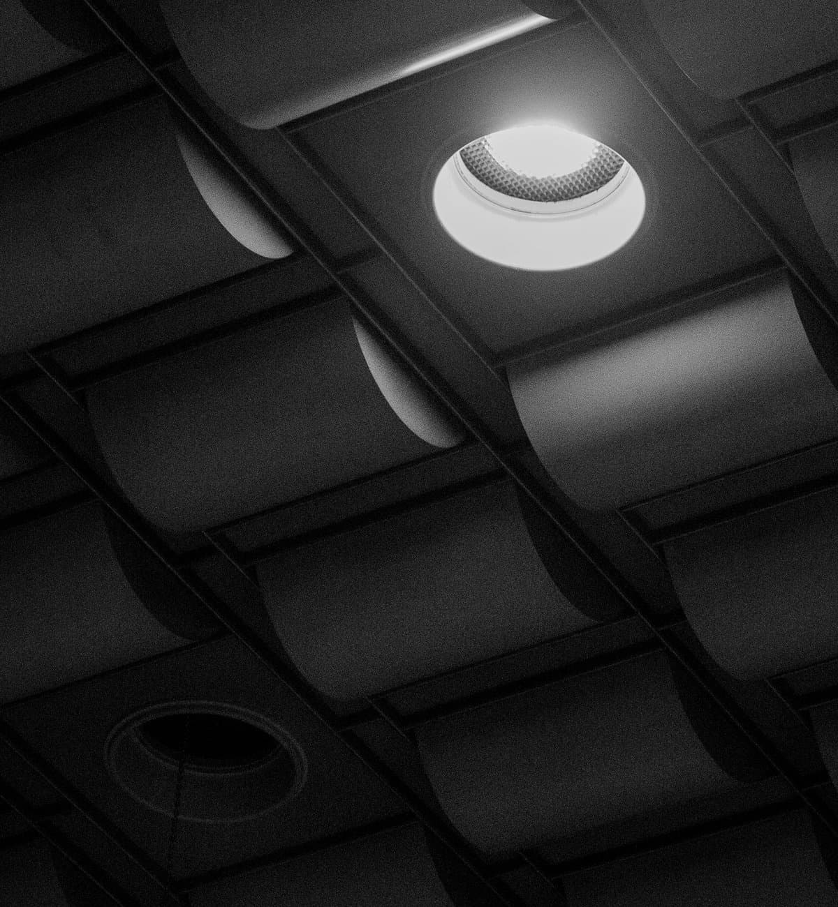 Recessed round downlight set into a dark coffered ceiling, photographed in monochrome